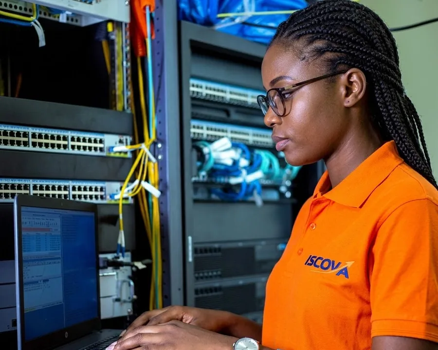 Une technicienne en polo ISCOVA travaille sur un ordinateur portable devant des armoires réseau
